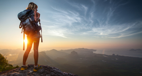 Lady hiker relaxing on top of hill and enjoying sunrise over the valley